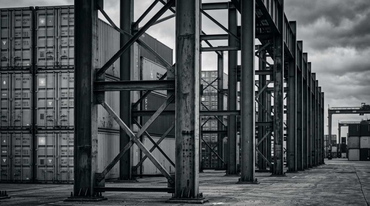 Container yard framed by heavy operational structure — enterprise operations managed across complex physical networks.